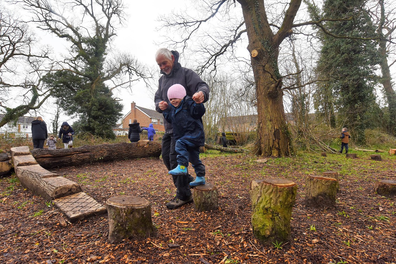Children playing balancing games at the Holbury Manor wild play site opening April 2018 An adult guides a child across wooden logs