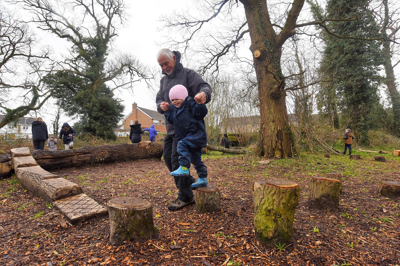 An adult guides a child across wooden logs