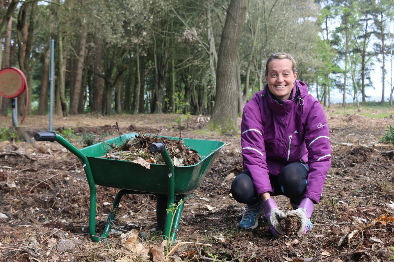 A woman looks at the camera as she places compost on the ground from a wheel barrel