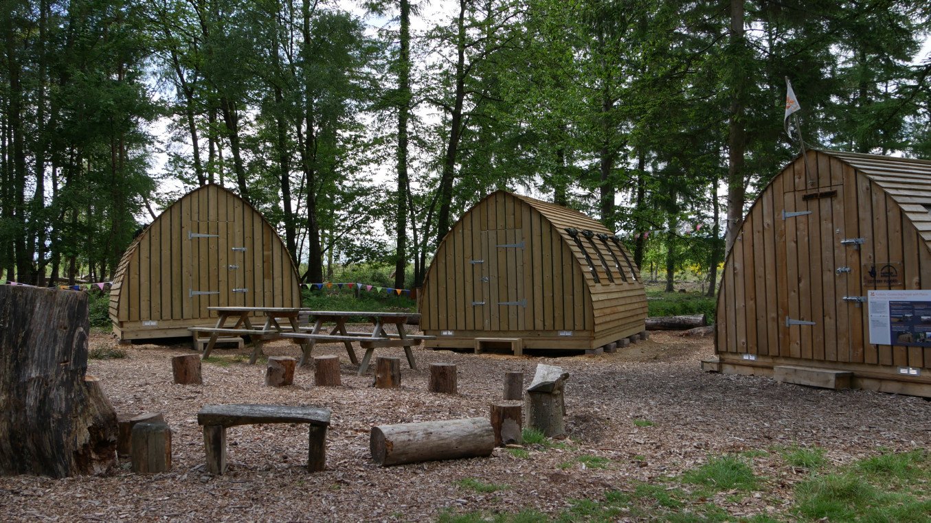 Foxbury basecamp Wood cabins and seating in a woodland scene