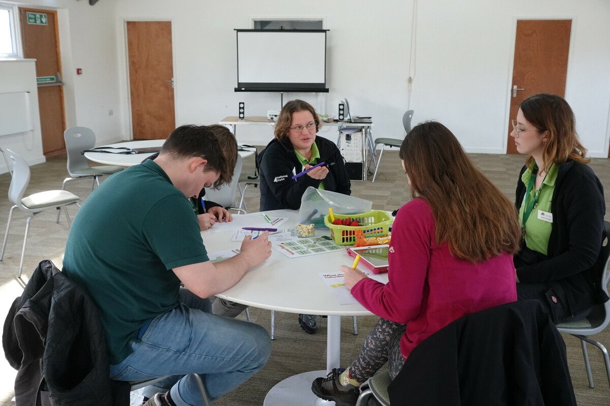 A group of young people sat around a table during a workshop on volunteering for 18-30 year olds led by the NPA education and youth team during the New Forest National Park Volunteer Fair 2024