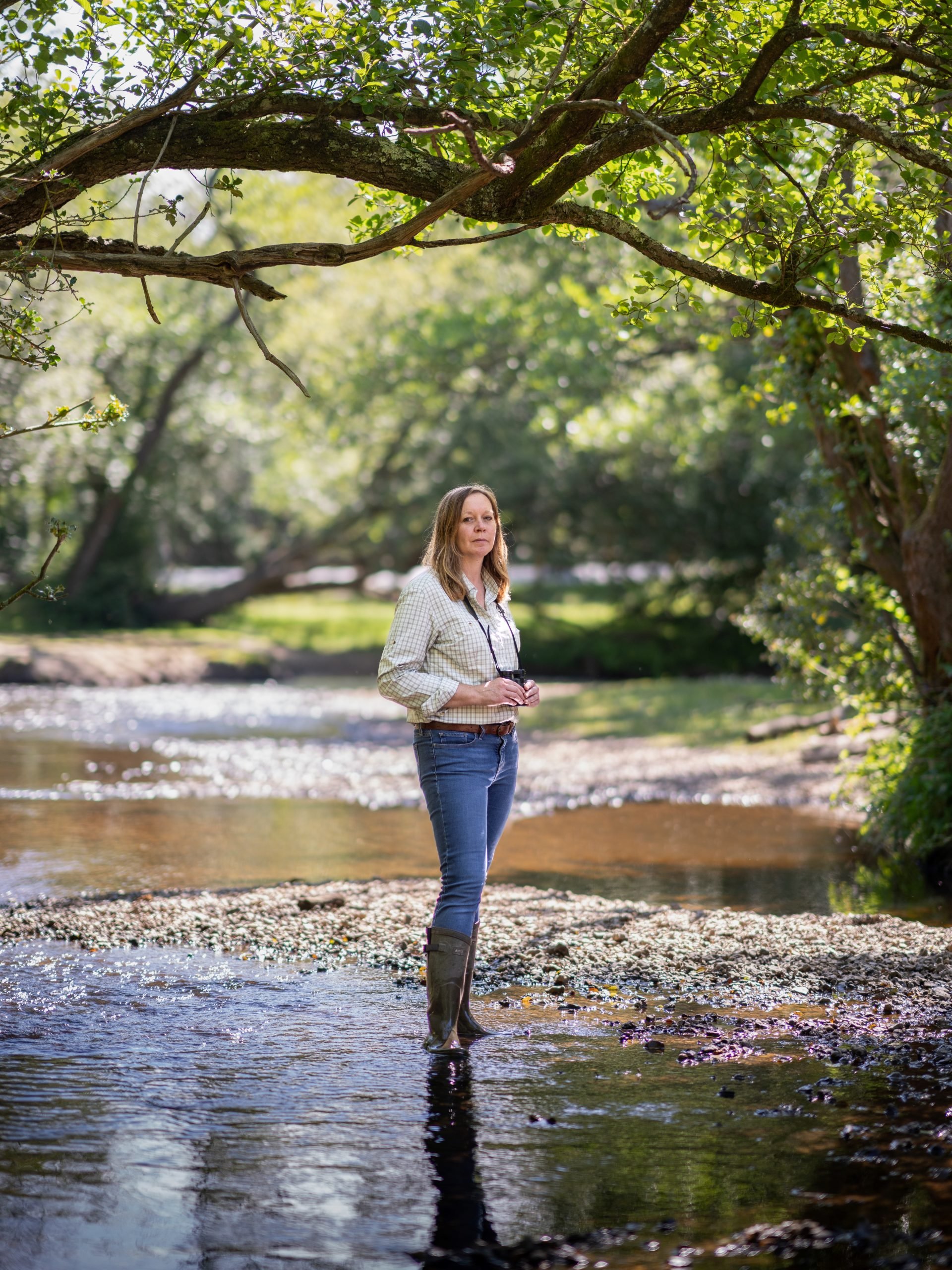 Forestry England ecologist Leanne Sargeant stood in a river holding binoculars