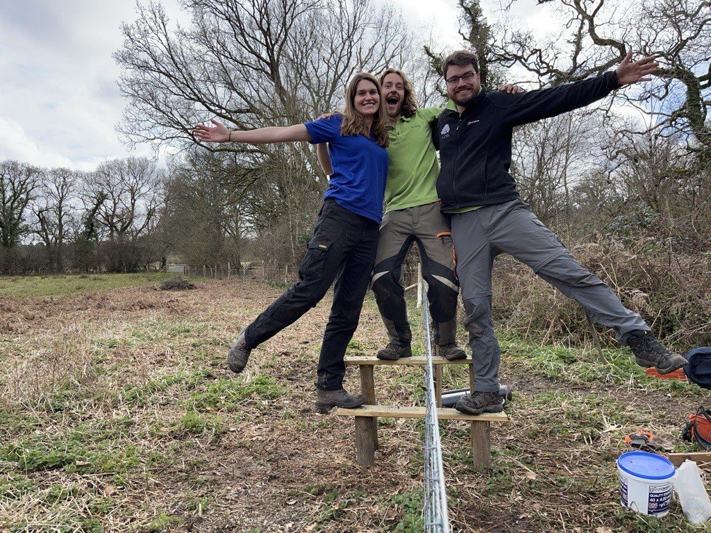 Former apprentice rangers Alistair and James with RSPB volunteer Maddie They are balancing on a beam and holding onto one another, laughing with arms outstretched