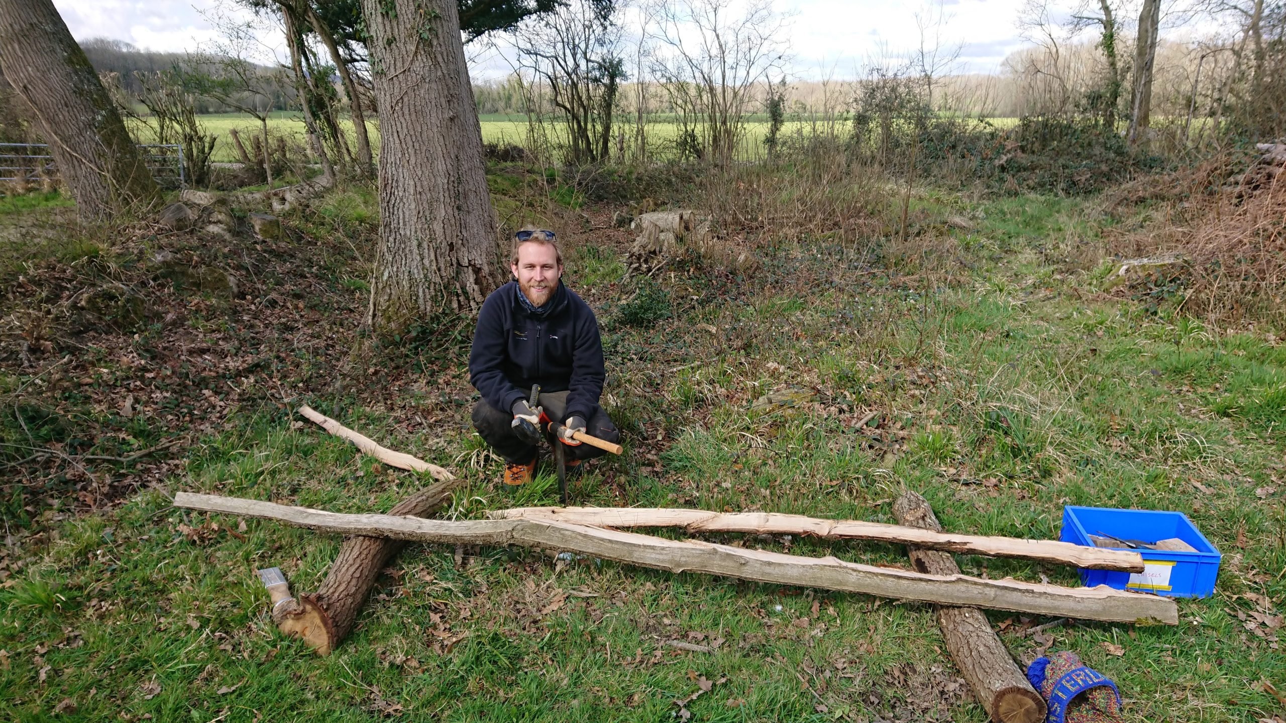 South Downs National Park ranger Jake crouches next to a split wooden rail