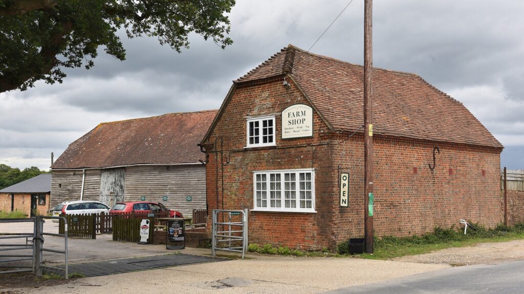 A red brick farm building with cars parked outside and signs saying farm shop and open
