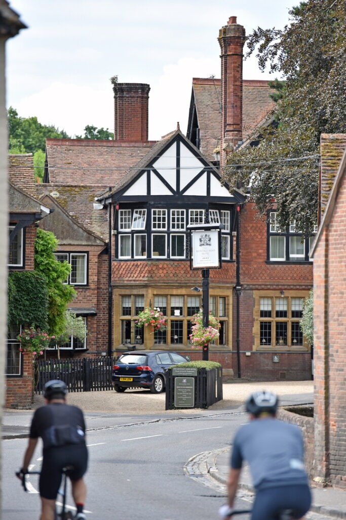 two cyclists on a road with a pub behind