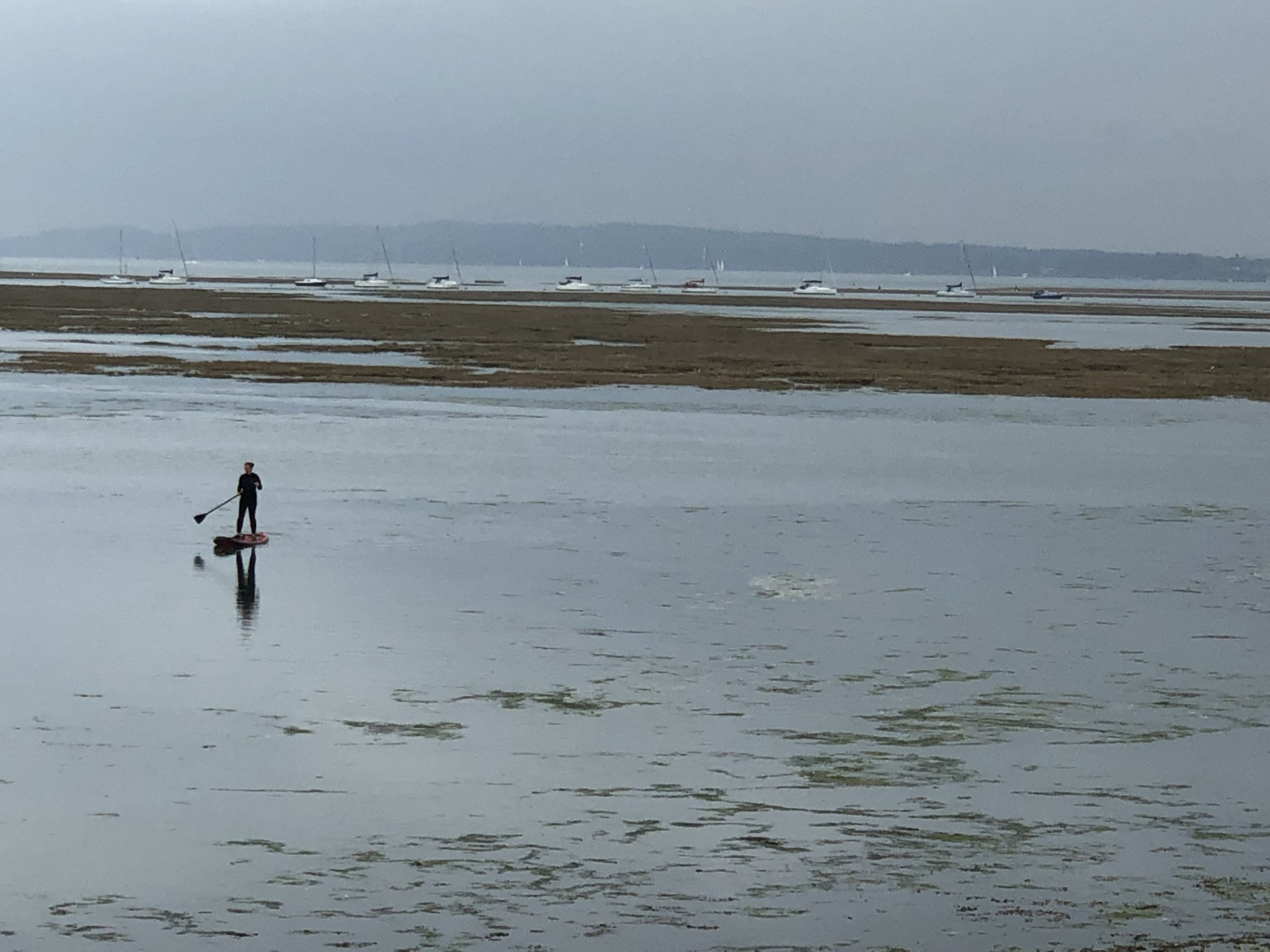 a paddleboarder with yachts behind