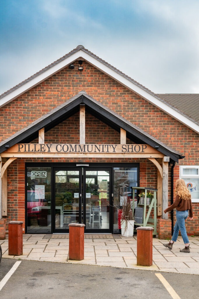 a person walking into a red brick building with a sign saying Pilley Community Shop