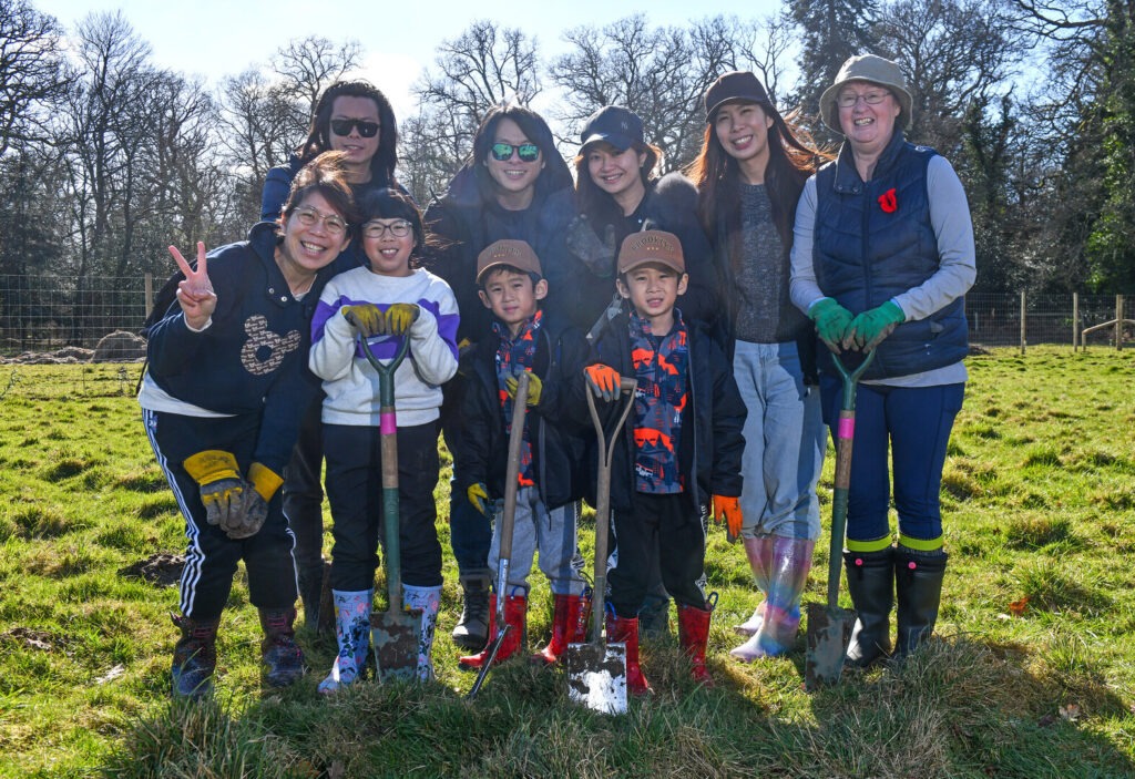 A group of adults and children holding spades and smiling at the camera