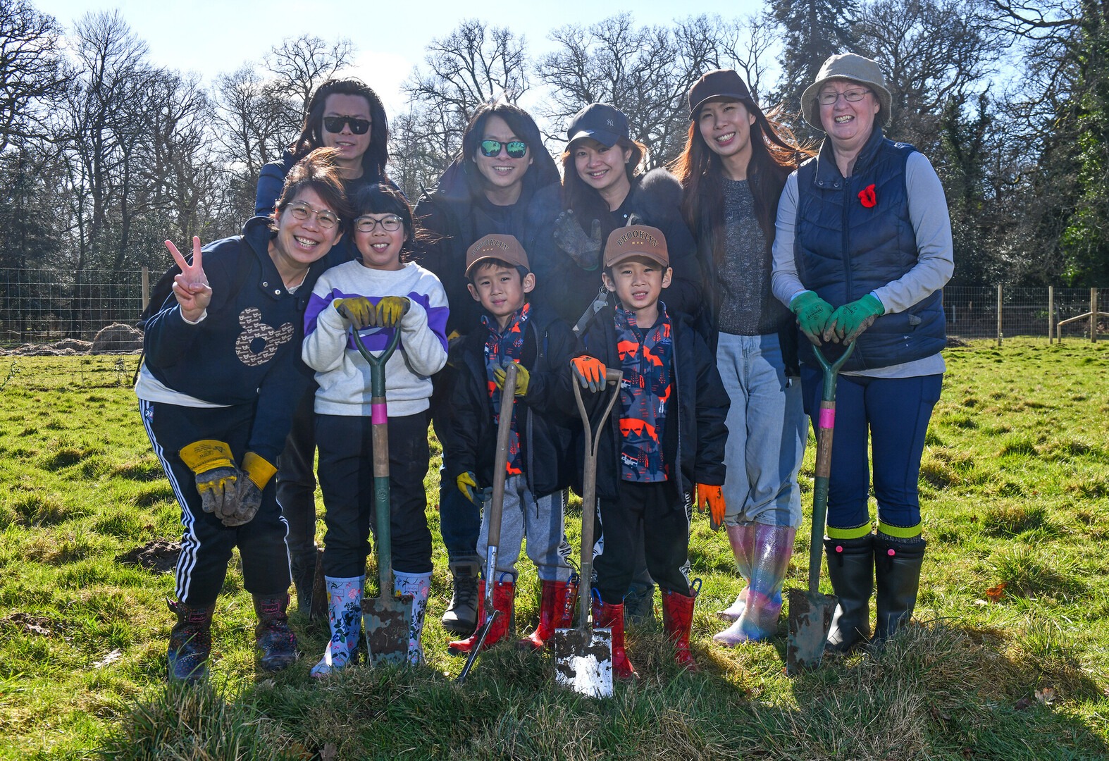 A group of adults and children holding spades and smiling at the camera