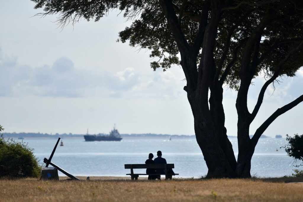 two people sitting on a bench overlooking a tanker at sea