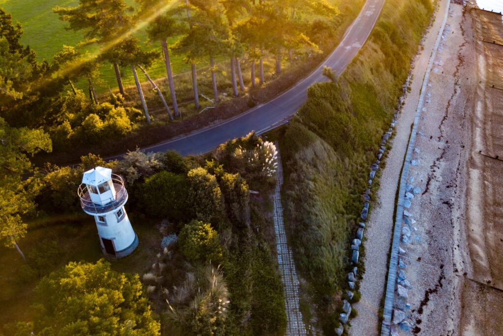 Overhead view of an inland lighthouse amid greenery with a beach nearby