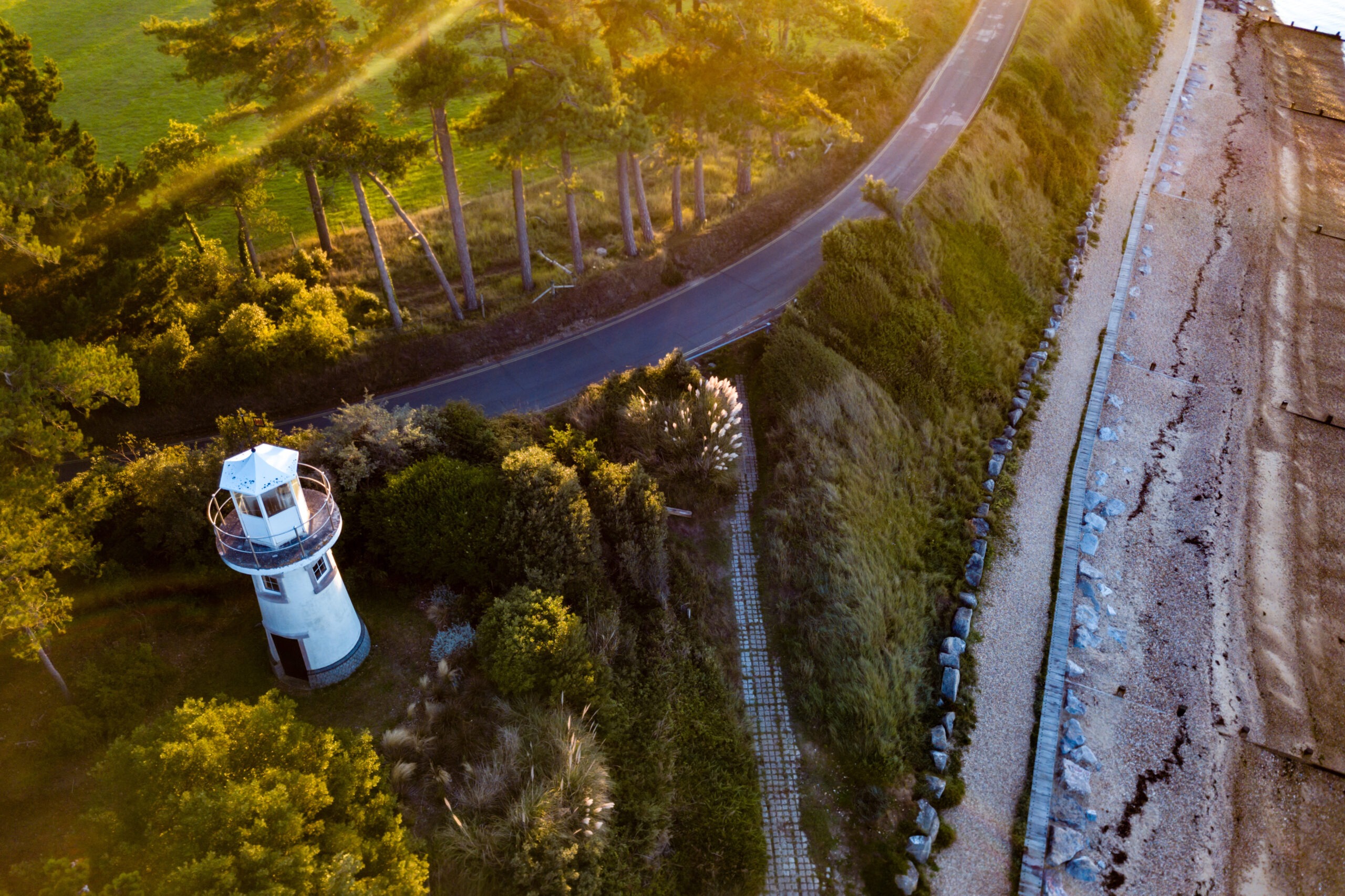 Overhead view of an inland lighthouse amid greenery with a beach nearby