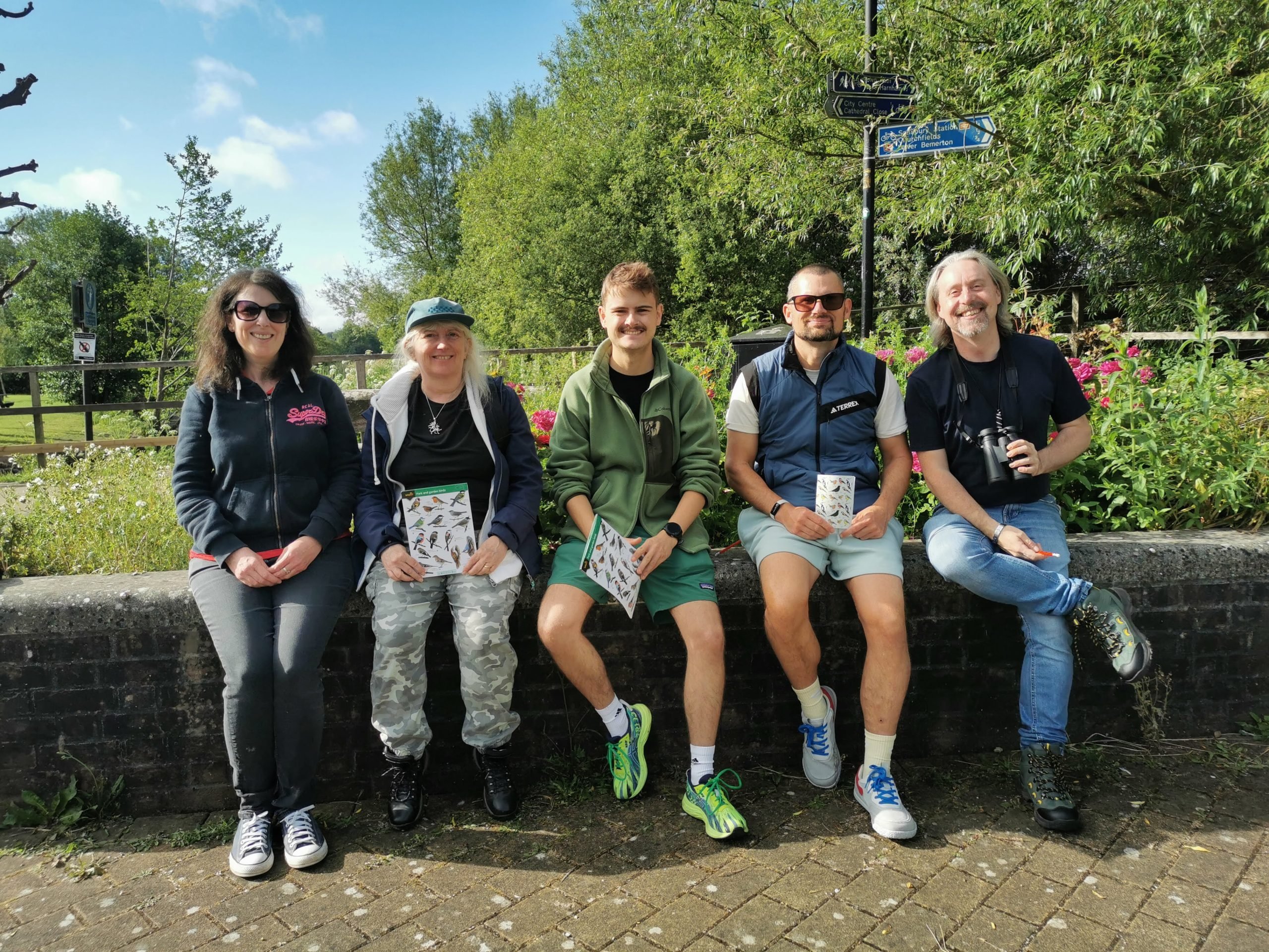 A group of people sat on a wall in a park with wildlife spotting guidebooks
