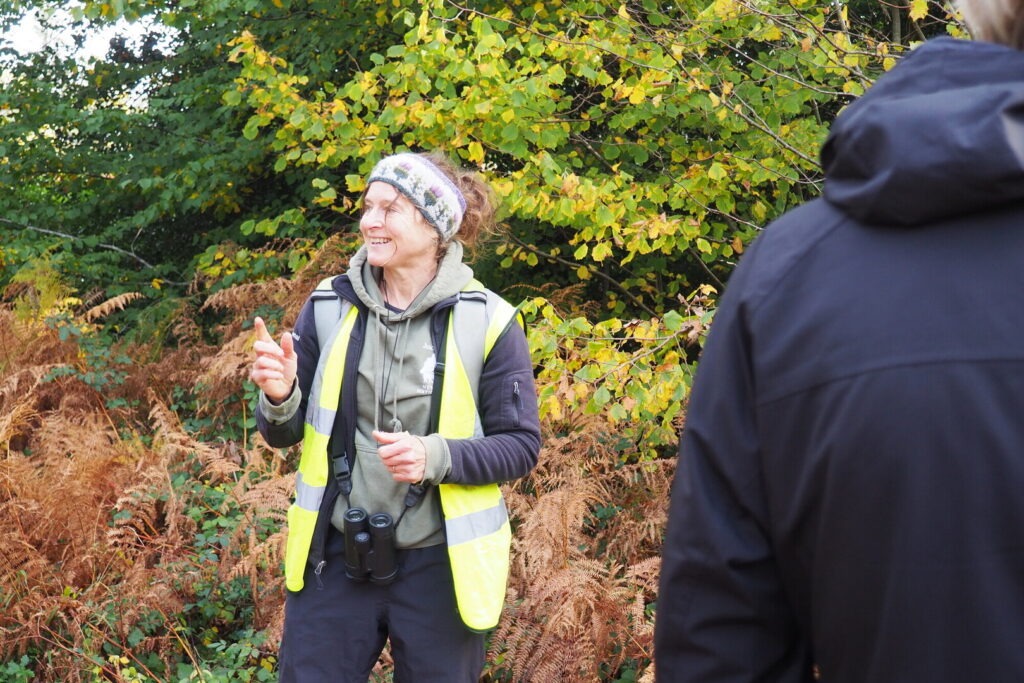 A woman in a high vis vest and headband talking to people in the outdoors