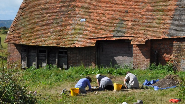 Group of people digging with hand tools in front of an old building