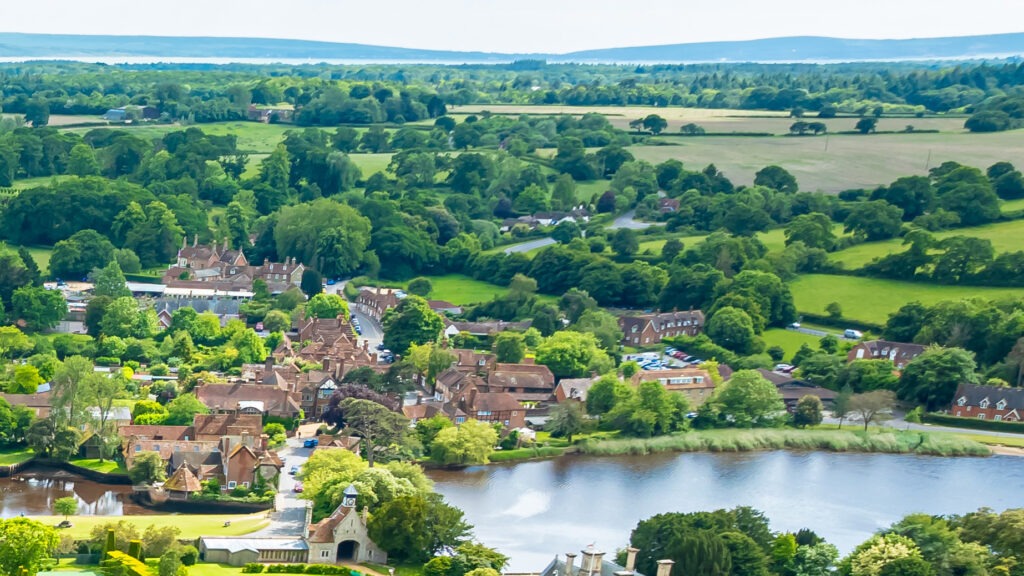 Aerial view of Beaulieu village with riverside buildings, a small church, and surrounding green fields and woodland