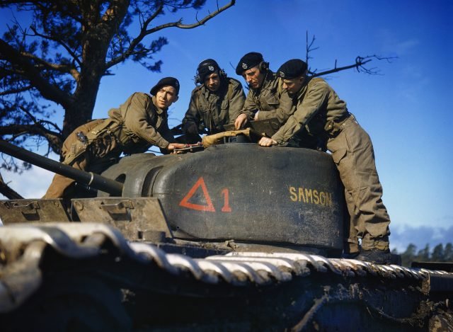 a group of WWII soldiers looking at a map on the turret of a tank