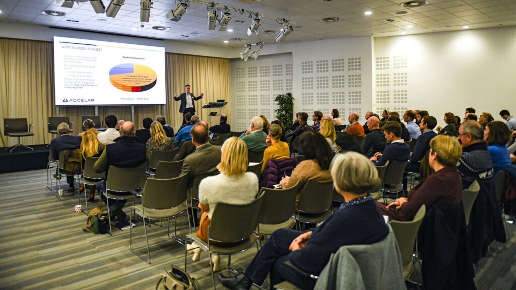 A goup of people sitting in a room listening to a person speaking with presentations slides