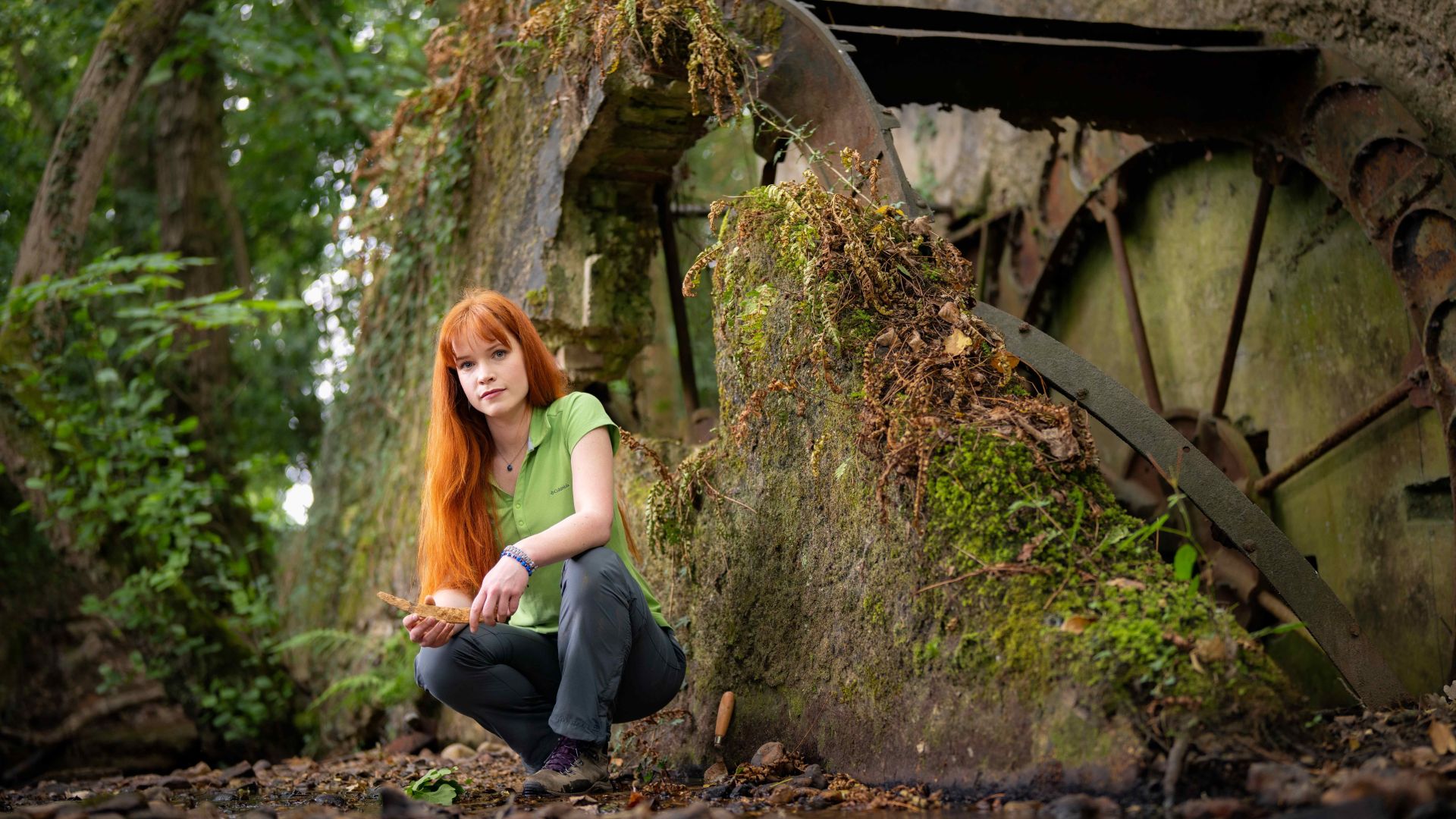 A woman crouching near an old water wheel