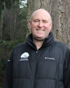 a person wearing a black gilet with a tree behind him