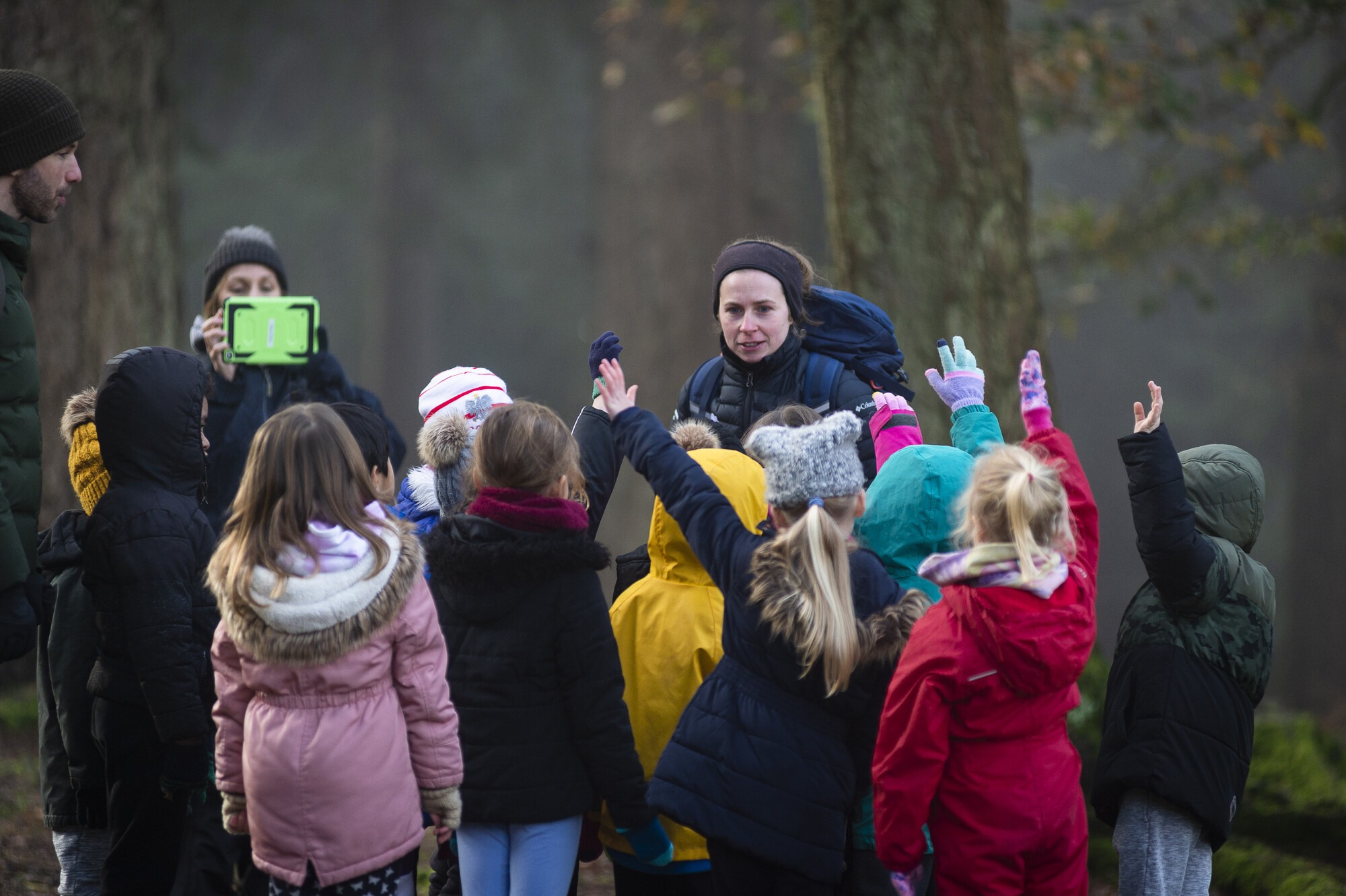 A group of primary school children gathered in front of a member of the NFNPA education and youth team. Some have hands up. They are stood in a wooded area and all wearing thick coats, some have hats, it appears to be winter.