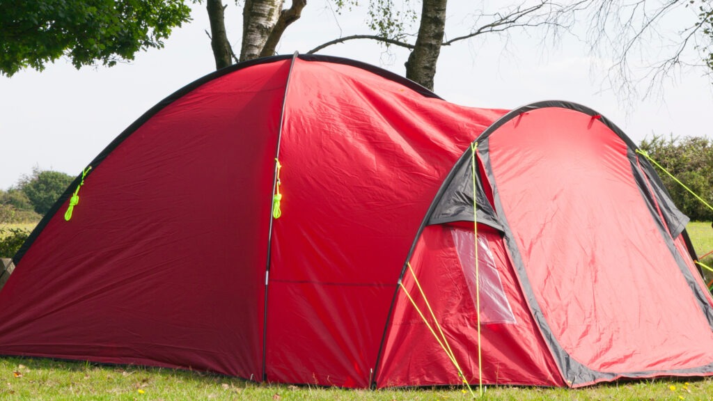 Colorful camping tent under the trees in rural settings, on a sunny summer day .