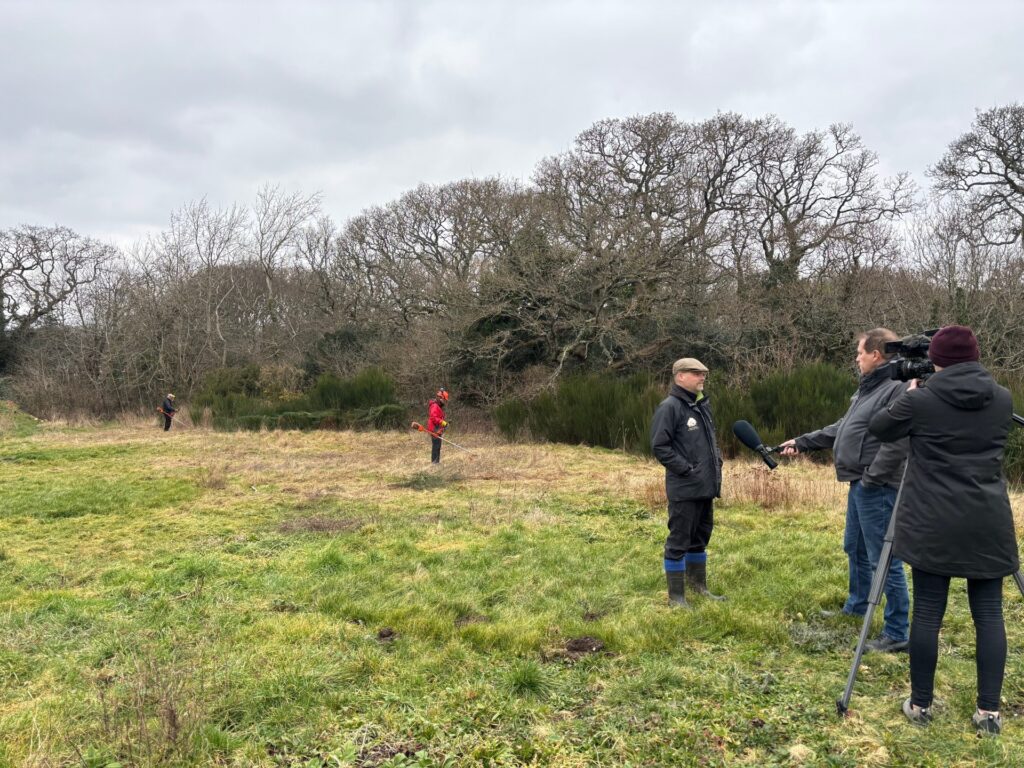 a person being interviewed in a field by a reporter with a microphone and camera person