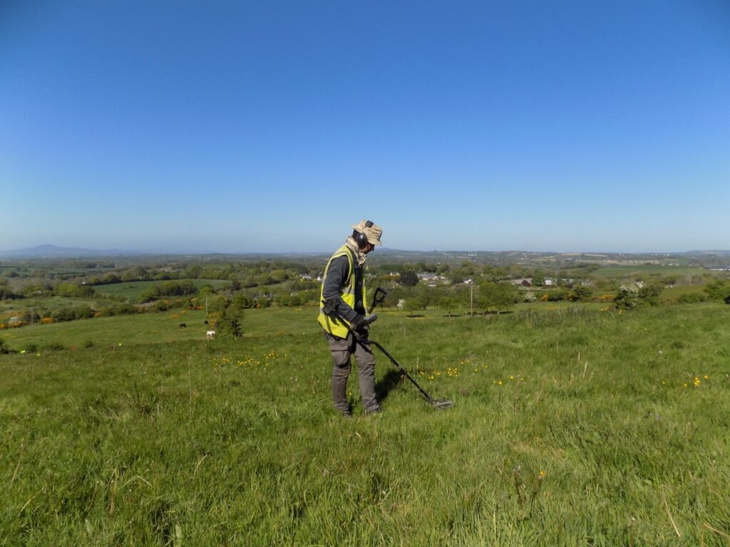 A man with a metal detector in a field on a sunny day