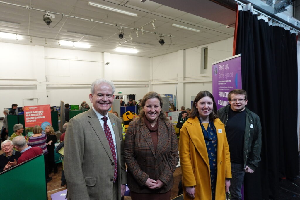 New Forest Youth Board members with two officials smiling on stage at the National Park Volunteer Fair 2025, with stalls behind