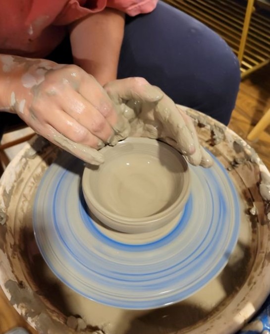 Hands shaping a small clay bowl on a spinning pottery wheel at a pop-up pottery session at Exbury