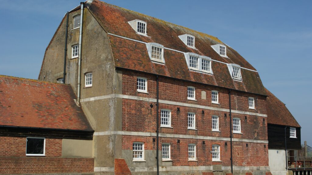 Ashlett Mill, a large red-brick building with a steep tiled roof and white dormer windows under a clear blue sky