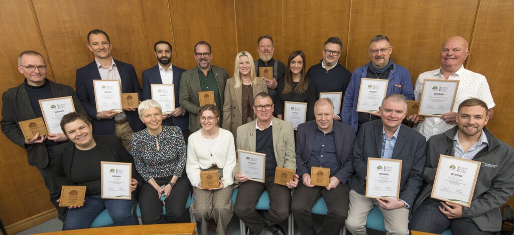 Group photo of New Forest Building Design Awards 2025 winners with NPA chair Victoria Mander, holding certificates and plaques