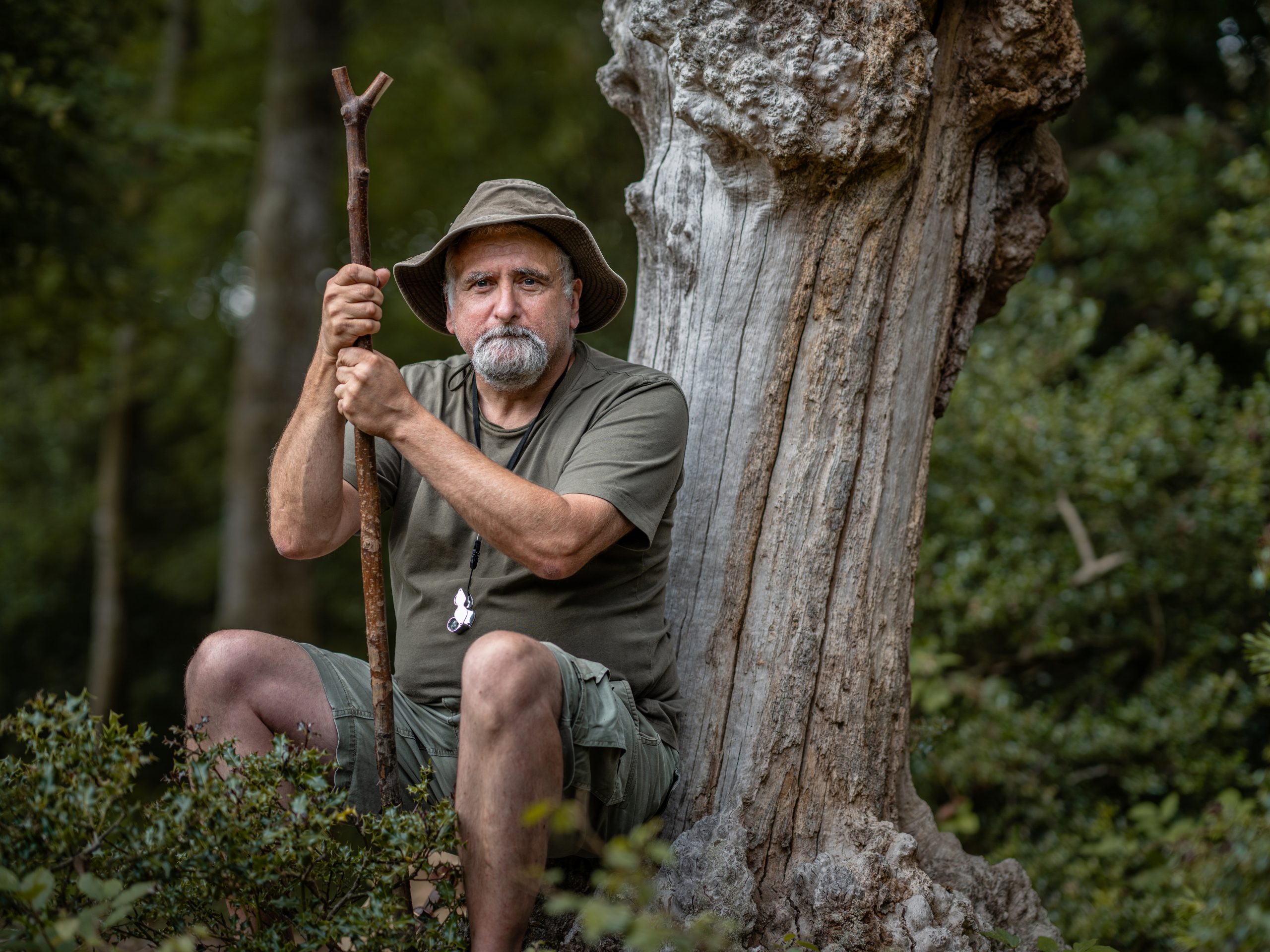 Conservationist and Verderer Clive Chatters crouching by a tree, he is holding a large stick for support