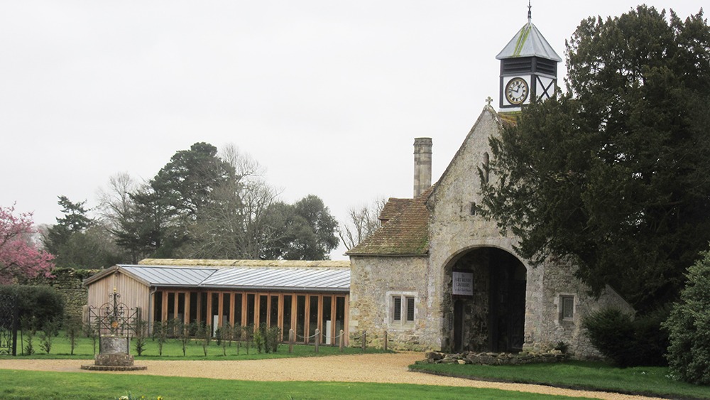 Stone gatehouse with arched entrance and clock tower at Beaulieu, beside a long wooden building and trees