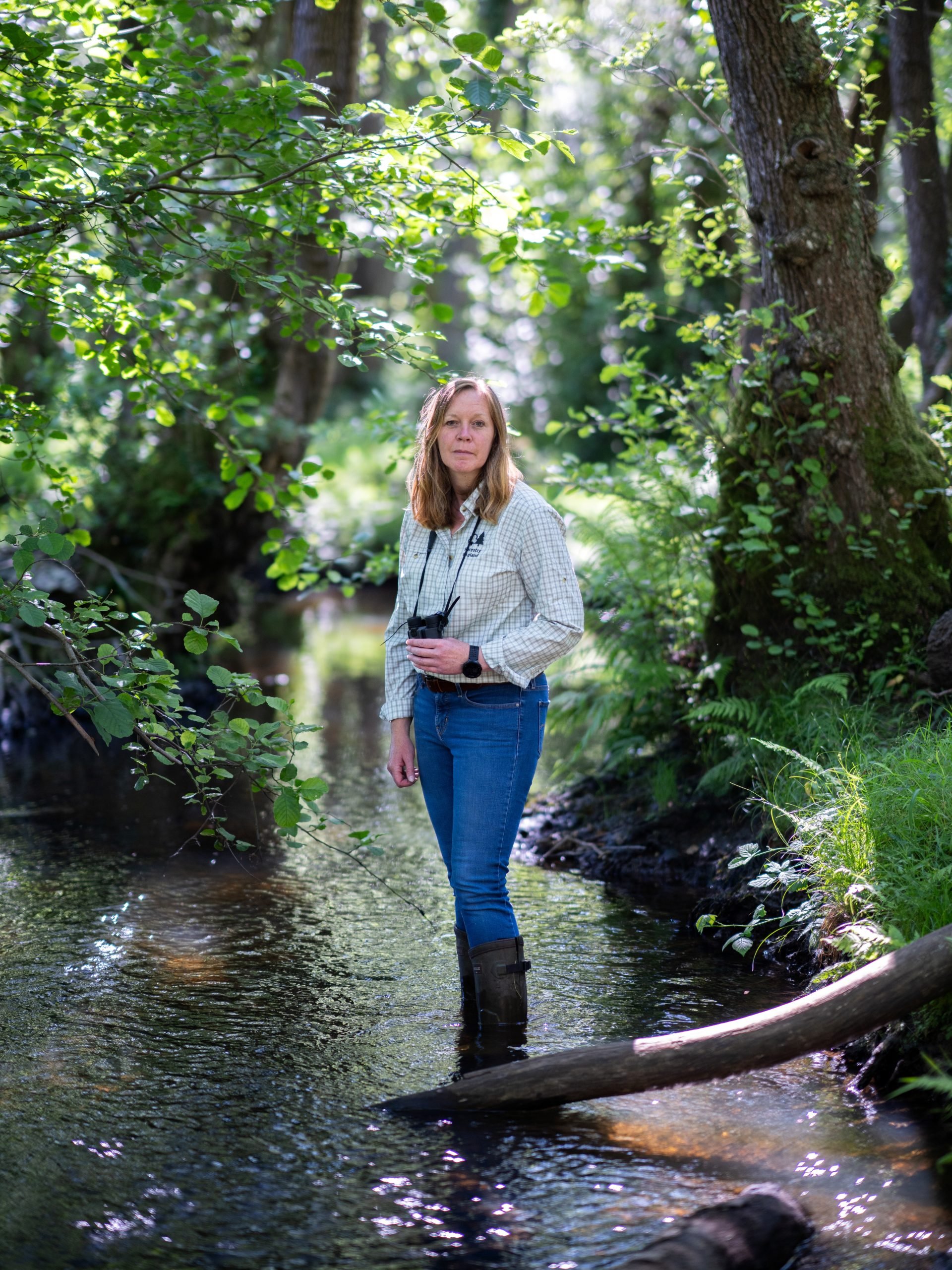Forestry England ecologist Leanne Sargeant stood in a river holding binoculars