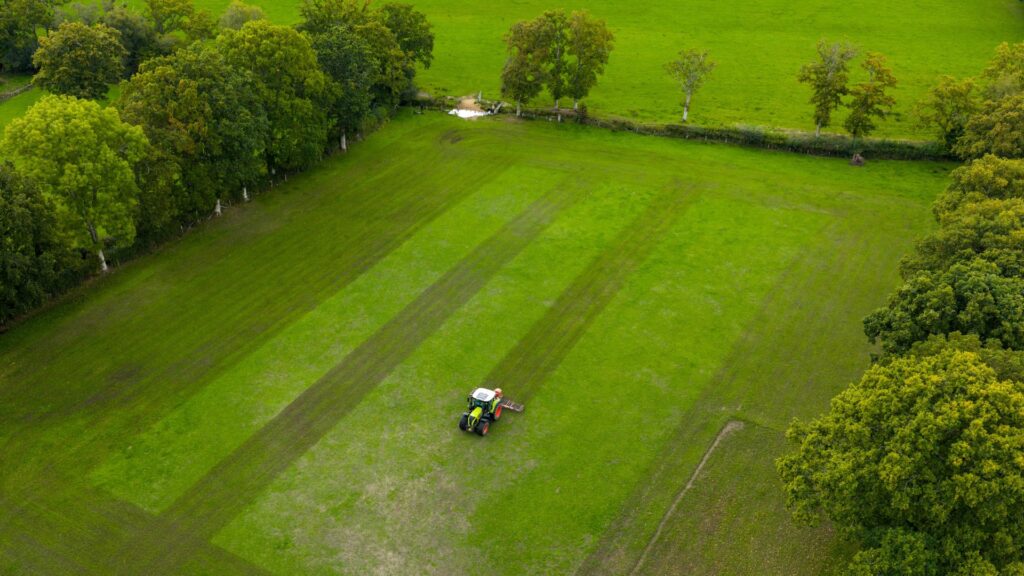 A tractor in a large green field with trees on the edge