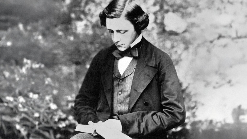 Black-and-white portrait of a young man in a suit and bow tie, seated outdoors and looking down at a book