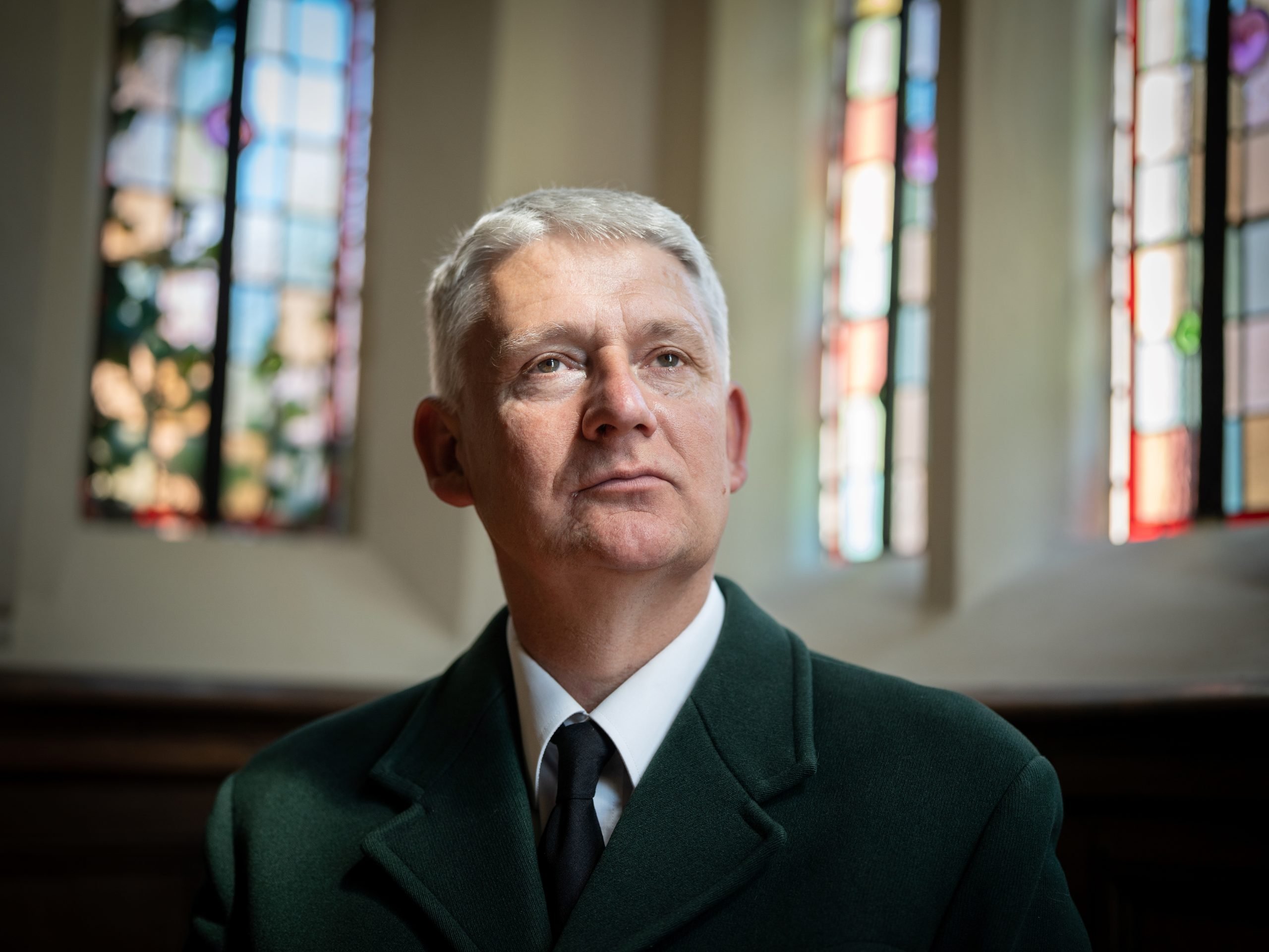 Head Agister Jonathan Gerrelli, a close up of his face, stain glass windows can be seen high on the walls behind him