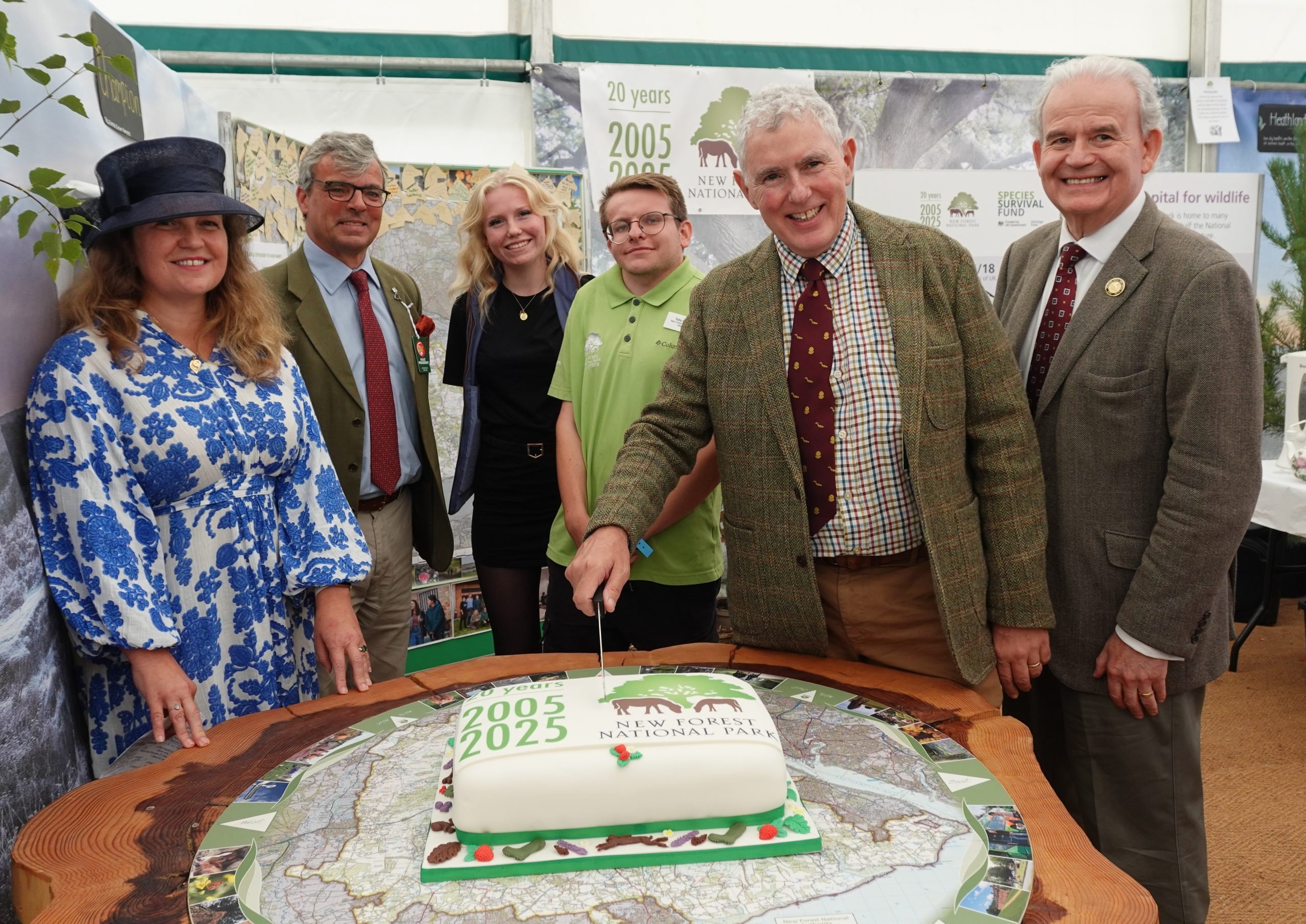 A row of people cutting a cake with the National Park logo on it in a marquee