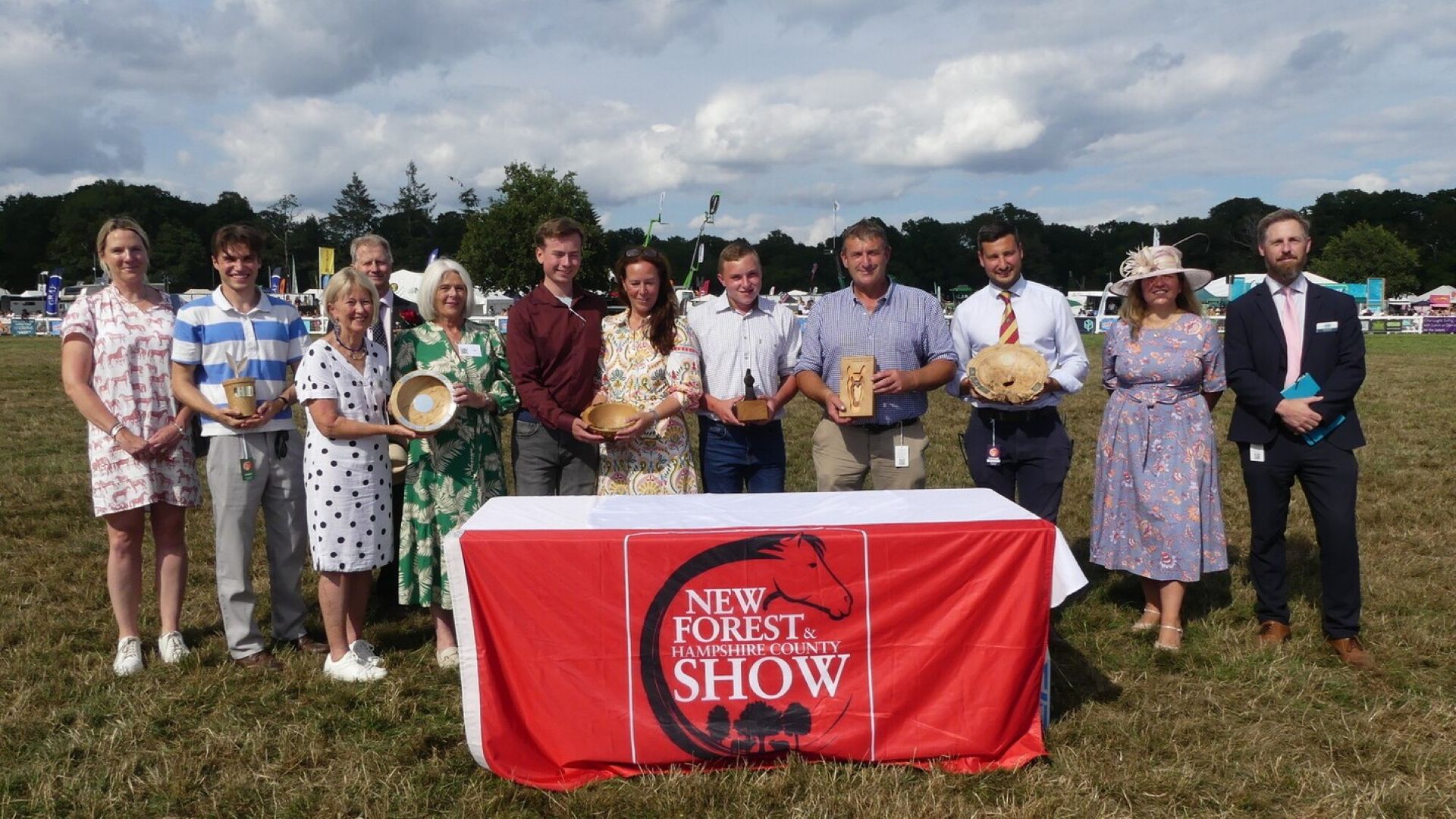 A row of people holding awards in front of a table with a cloth saying New Forest Show