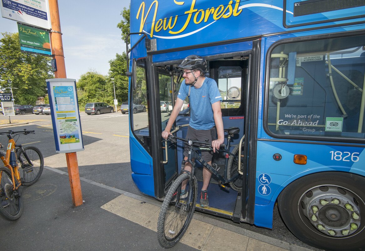 A man wearing a helmet and wheeling his bike off of the blue New Forest Tour bus