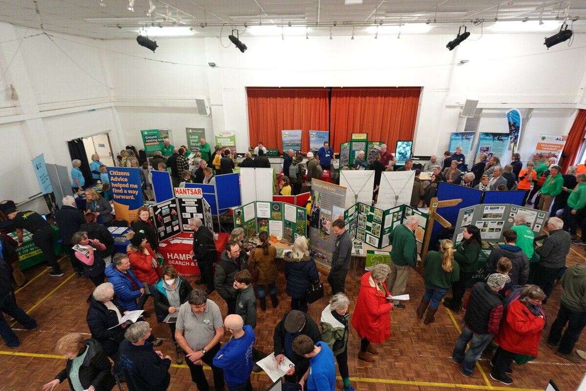 The New Forest National Park Volunteer Fair 2024. Photo taken from above showing many people in Brockenhurst Village Hall browsing stalls of different charities and organisations