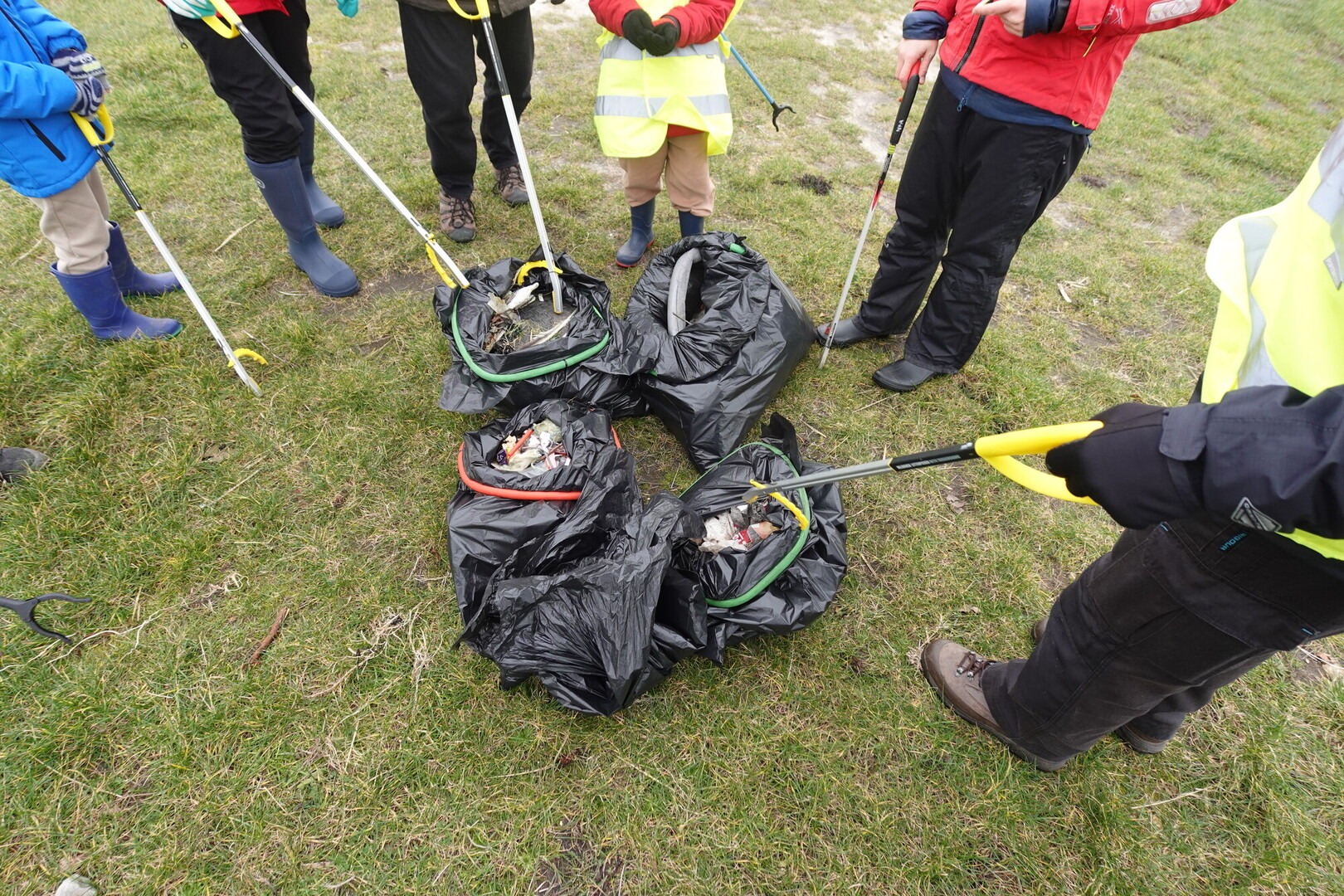 A group of people with litter pickers stand in a circle around black bags full of rubbish on a litter pick.