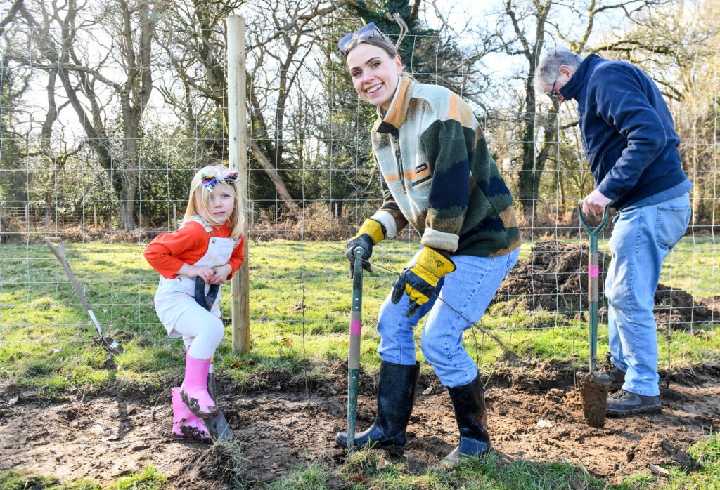 Two people - a woman and a girl - stand in a field taking part in a community tree planting event.