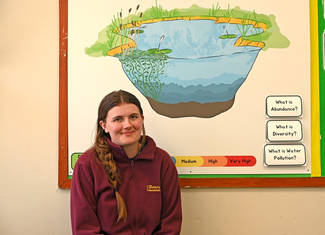CET intern Alex in front of a poster explaining pond life