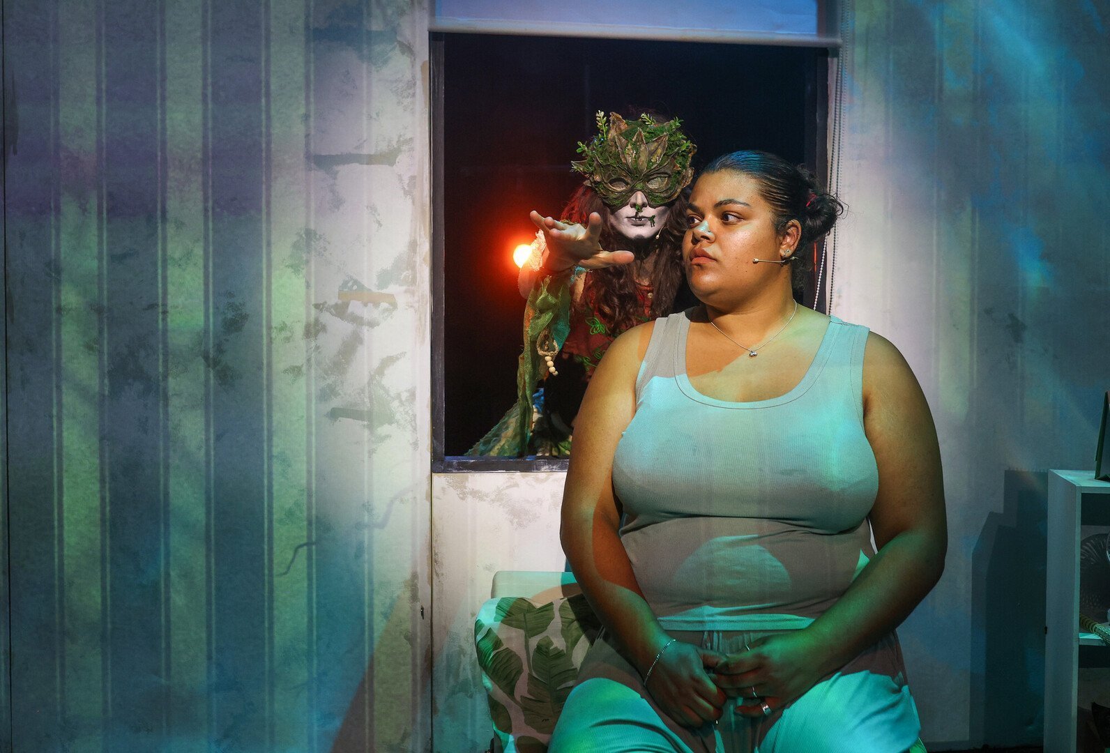 A scene from a play. A woman sits by a window and a mythical giant appears to be reaching over her shoulder.