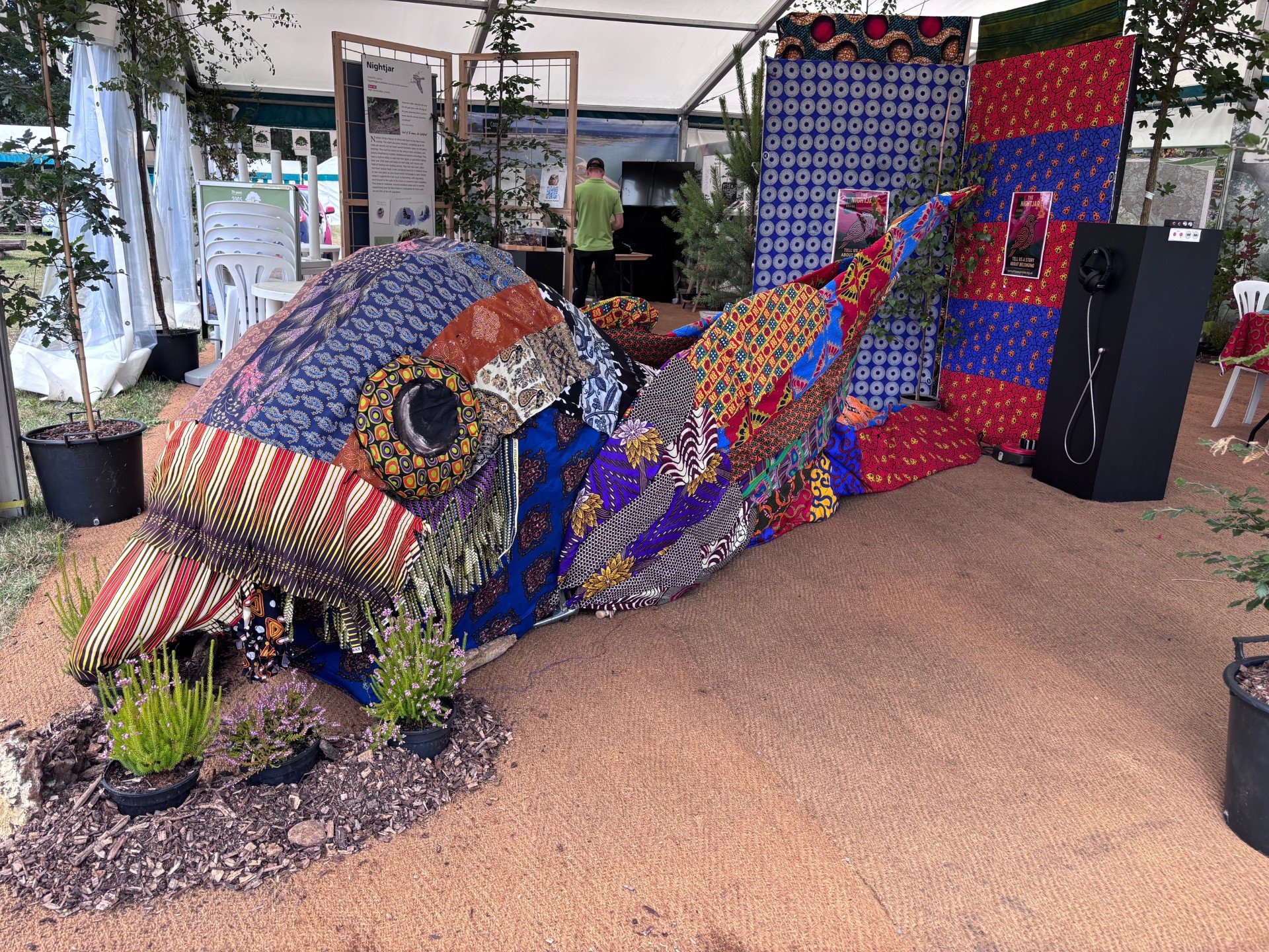 An art installation of a nightjar bird covered in vibrant textiles in a marquee at an event.