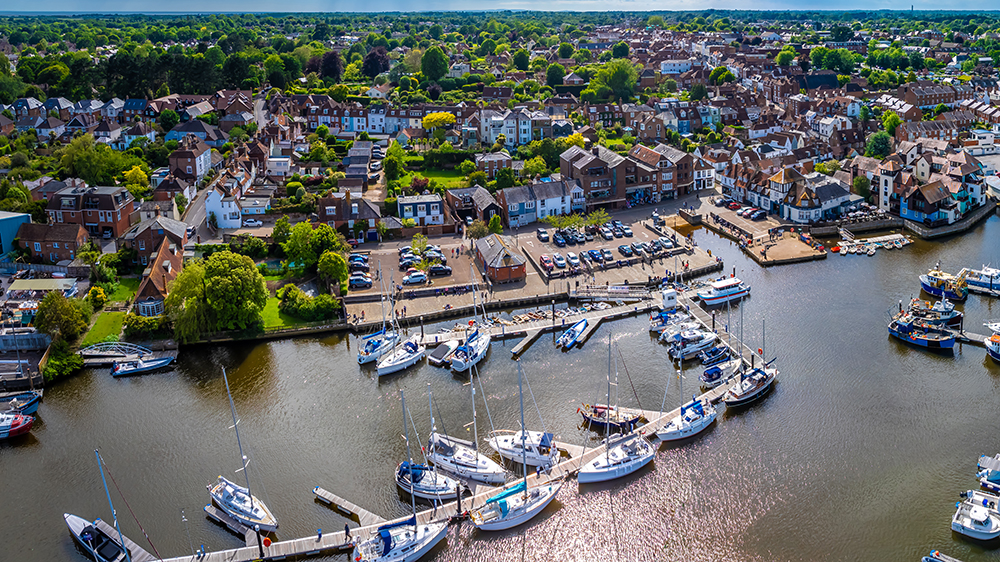 Aerial view of Lymington marina with moored sailboats, riverside quay, car park, and dense townhouses behind