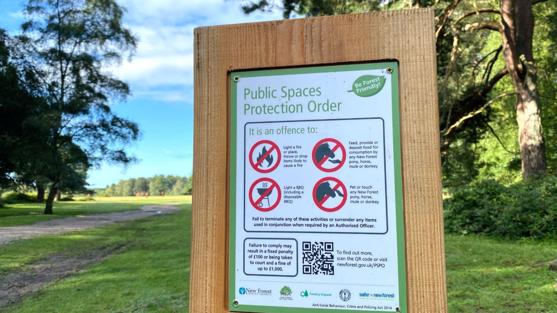 A poster in a wooden frame in a grass and woodland setting outlining the PSPO rules in the New Forest